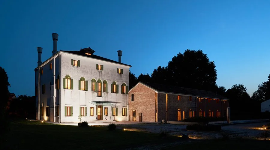 La villa illuminata di notte, accanto alla barchessa in mattoni.