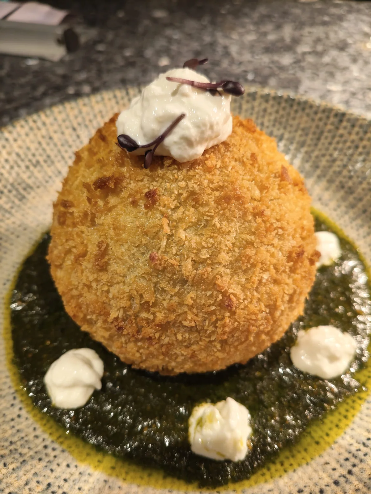 Arancino siciliano dorato adagiato su una crema al basilico