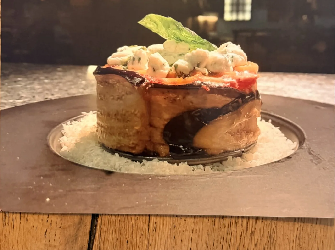 Parmigiana di melanzane servita in altezza, con erborinato e basilico.