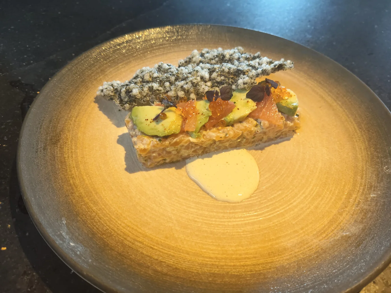 Battuta di salmone e avocado a strati con cialda croccante su piatto dorato